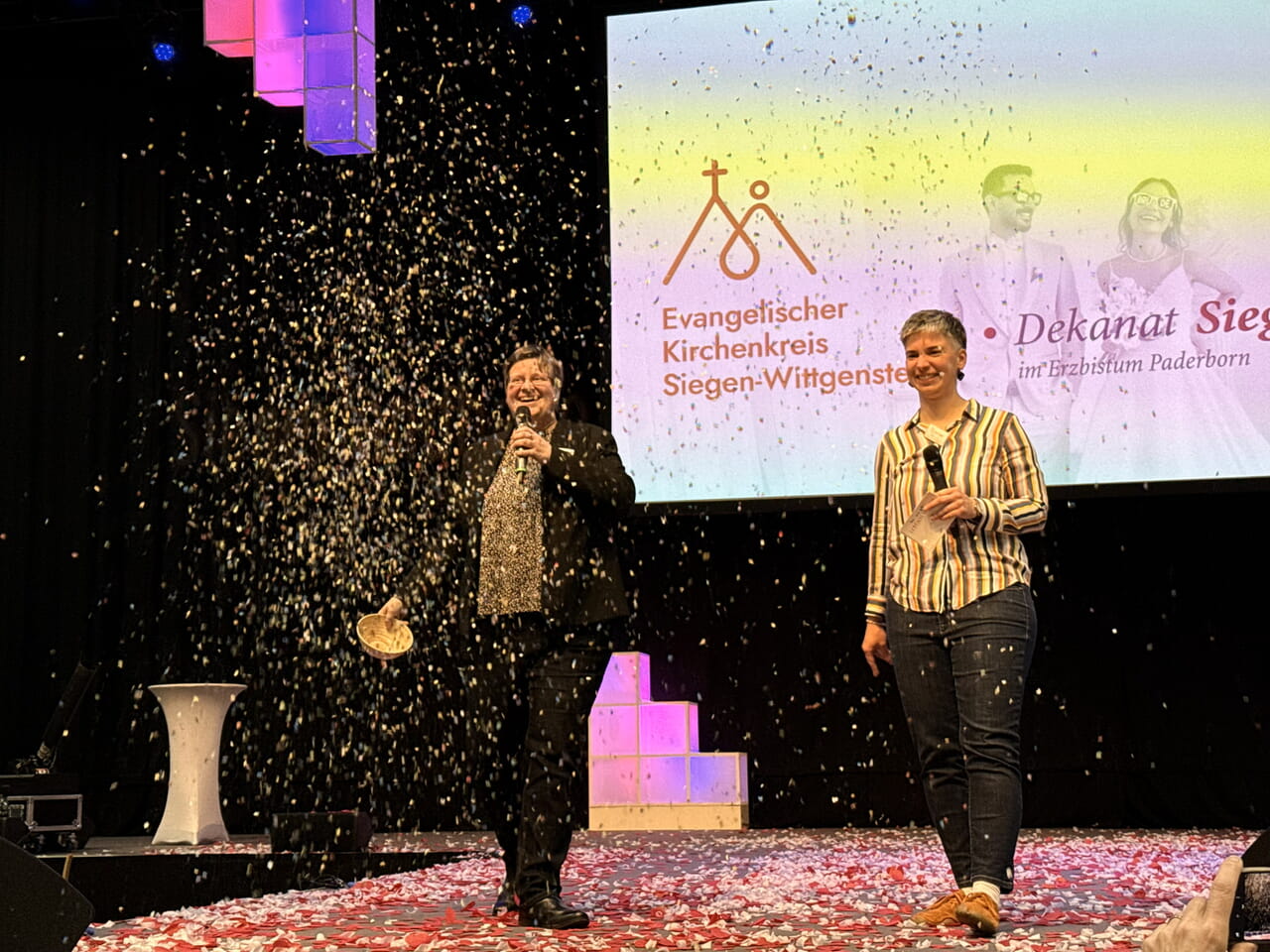 Alexandra Podstawa und Carmen J&auml;ger lassen Konfetti auf die Zuschauerinnen und Zuschauer regnen und laden zum &ouml;kumenischen Stand ein.