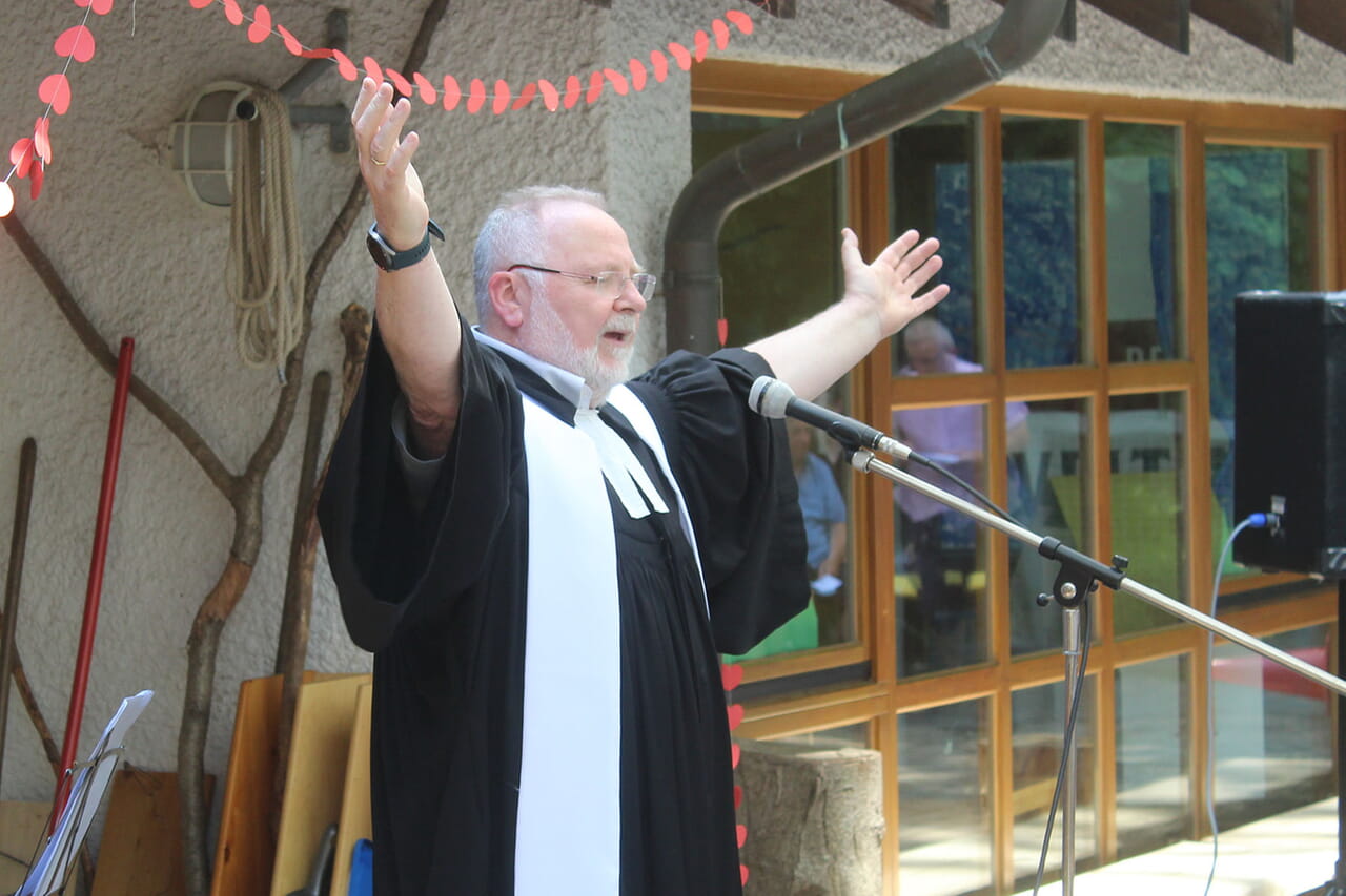 Große Gesten des Pfarrers Armin Pulfrich und kleine rote Herzen an der Girlande über ihm charakterisierten das Tauffest der Siegener Lukas-Kirchengemeinde nahe der Erlöserkirche sehr gut.