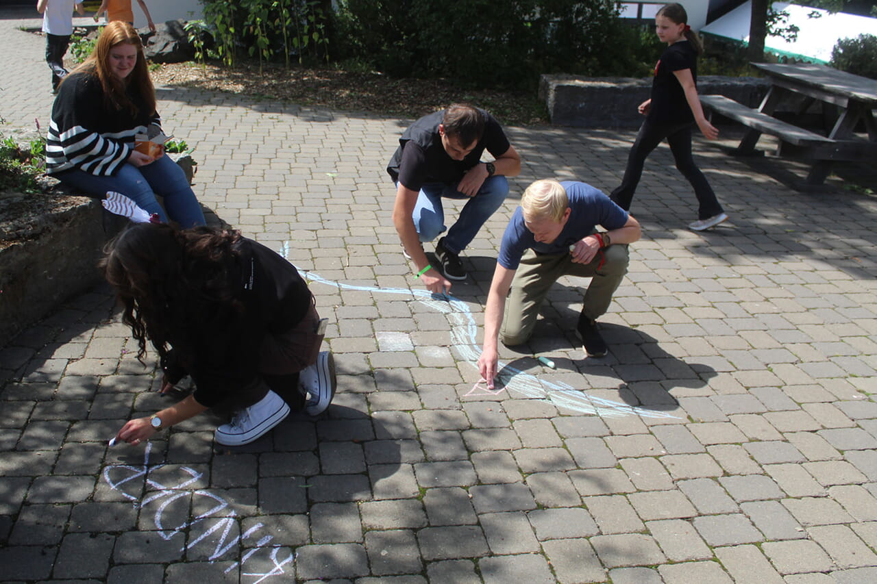 Auch ein Mitarbeitenden-Team nahm bei der Wittgensteiner Ferienspiele-Freizeit am Chaosspiel teil, ihre Aufgabe: mit Kreide ein Bild vom Abenteuerdorf malen.